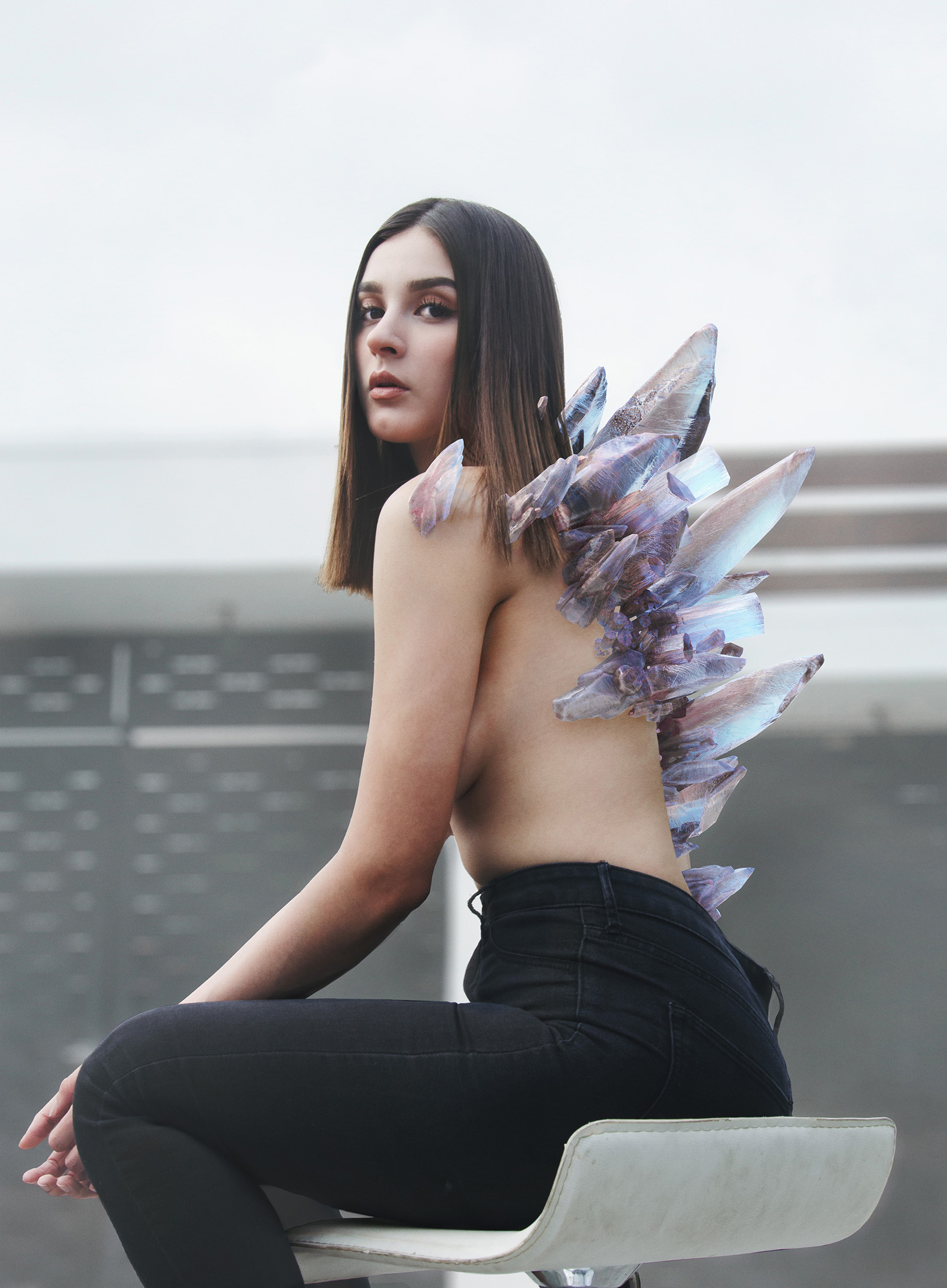 Cassandra Villareal sits on a white stool her back adorned with shimmering crystals against a modern architectural backdrop.